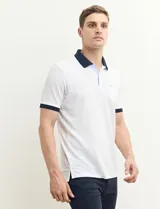 Remera polo blanca de piqué con cuello y puños en azul marino. Tiene tapeta de dos botones y bolsillo de parche en el pecho.