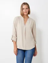 Blusa de gasa color beige, con cuello a la base y escote en V. Manga larga con presilla y botón para ajustar el largo.