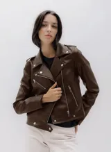Campera estilo biker de efecto cuero color marrón oscuro, con cierre frontal de cremallera asimétrico, solapas anchas con broches metálicos y múltiples bolsillos con cremallera. Posee charreteras en los hombros y un cinturón incorporado en el ruedo.