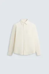 Camisa color crema de corte relaxed fit, confeccionada en tejido de algodón con acabado cepillado. Tiene cuello solapa, manga larga con puño abotonado, bolsillo de parche en el pecho, efecto lavado y cierre frontal con botones.