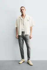 Pantalón de jean negro ajustado al cuerpo desde la cintura hasta el tobillo, de tiro medio y tejido elástico. Diseño de cinco bolsillos con lavado efecto roto y cierre frontal con cremallera y botón.