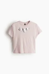 Remera corta de algodón color rosa con cuello redondo y estampado plateado en el frente.