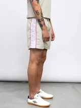 Short de baño color beige con cintura elástica ajustable con cordón, bolsillos laterales y logo Umbro estampado en el lateral de la pierna izquierda.