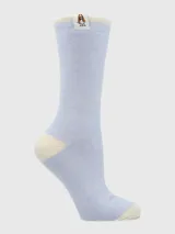 Calcetín de largo medio, tejido grueso, color celeste claro jaspeado, con talón y puntera en color crema. Presenta una etiqueta tejida con el logo de un perro (Basset Hound) en el borde superior.