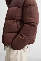 Campera puffer marrón con cuello alto, cierre frontal con cremallera, bolsillos laterales y puños elásticos.