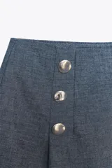 Bermuda azul de tiro alto confeccionada con lino. Presenta detalle de falsos botones y pinzas delanteras, falsos bolsillos de vivo en espalda y cierre lateral con cremallera oculta en costura.