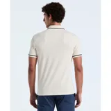 Polo color crema de algodón piqué, con cuello tipo camisa y cierre de botones. Tiene mangas cortas con ribete negro, bolsillo de parche en el pecho y logo bordado de pingüino.