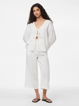 Blusa blanca de algodón con escote en V y mangas largas abullonadas. Presenta cierre frontal con lazos.