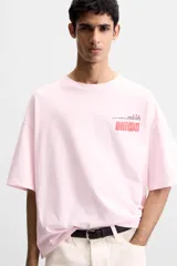 Camiseta rosa de corte holgado, cuello redondo y manga corta. Estampado frontal con texto en rojo "Amalfi Coast" y estrellas.