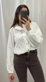 Camisa blanca con estampado de flores pequeñas, cuello mao, mangas largas abullonadas con puños elásticos y cierre frontal con botones.