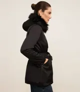 Campera parka negra con cuello alto, capucha con borde de piel sintética, cierre frontal con cremallera, bolsillos con cremallera y cinturón con hebilla.