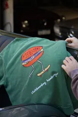Buzo verde con estampa de una hamburguesa andando en skate y la frase "skateboarding hamburger".