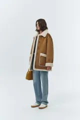 Chaqueta reversible de cuero sintético color marrón con forro de corderito sintético blanco. Presenta cuello de solapa, cierre frontal con botones, bolsillos de parche y detalles de corderito en puños, bolsillos y bordes.