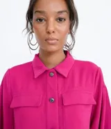 Campera color fucsia de crepe con cuello de camisa, manga abullonada, cierre frontal con botones y bolsillos frontales aplicados.