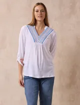 Blusa blanca de poliéster y rayón con escote en V bordado y mangas tres cuartos regulables con presilla y botón.