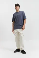 Remera de manga corta color crudo, corte oversize, con estampa en la espalda que incluye flores rojas, texto con el nombre de la marca y la frase 'The Art Society'.