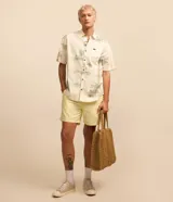 Camisa de manga corta con estampado de palmeras y motivos playeros en tonos celeste y verde sobre fondo blanco.