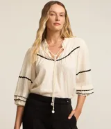 Blusa color crema de tricolina con detalles de ondas negras en cuello, mangas y frente. Tiene mangas 3/4 con volados y lazo en el cuello.