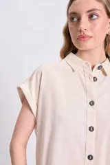 Camisa color crudo de lino, con cuello clásico, manga corta con dobladillo y cierre frontal con botones negros.