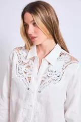 Vestido camisero corto color crudo, de lino, con cuello camisero, mangas largas y cierre frontal con botones. Presenta apliques de encaje en cuello y hombros.