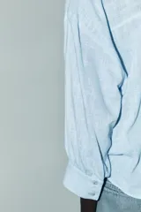 Camisa blanca de cuello solapa y manga larga con puños. Tiene un nudo en la parte delantera y cierre frontal con botones.
