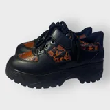 Zapatillas negras con detalles en animal print naranja y cordones negros.