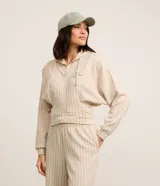 Campera deportiva color beige con rayas verticales finas, corte oversized, capucha con cordón ajustable, cierre frontal con cremallera, estampa bordada en el pecho, mangas largas ajustadas y bajo ajustado.