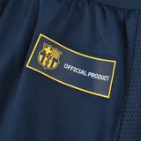 Short deportivo azul marino con cintura elástica y cordón ajustable. Presenta el escudo del FC Barcelona en la pierna derecha y la inscripción "Barça" en la pierna izquierda.