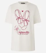 Remera color crudo de algodón, con cuello redondo y mangas cortas. Estampa frontal con dibujo de zapatillas de ballet, corazón y texto "La Coquette avec tout mon amour".
