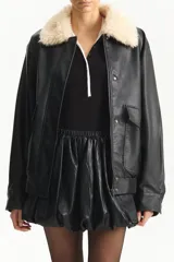 Chaqueta estilo aviador de cuero sintético negro, con cuello de pelo sintético color crema. Presenta cierre frontal y bolsillos con solapa en el pecho.