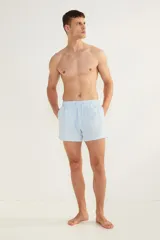 Short de baño celeste con rayas verticales blancas, de sirsaca, con aberturas laterales cortas, elástico en la cintura con cordón ajustable, bolsillos laterales y bolsillo trasero con cierre autoadherente. Suspensor interior de malla.