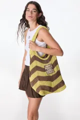 Bolso tejido a crochet con diseño a rayas horizontales en color amarillo y marrón. Tiene dos asas de hombro y un parche con el logo de "The Flowers Club".
