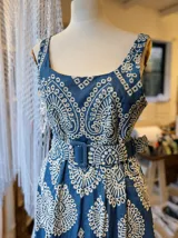 Vestido de jean azul con bordado floral blanco, corte midi, breteles anchos y cinturón con hebilla forrada.