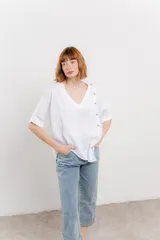 Blusa color naranja confeccionada en 100% lino, con escote en V, mangas cortas con vuelta y silueta amplia. Presenta terminación asimétrica y fila de botones decorativos en uno de los hombros.