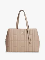 Cartera Tommy Hilfiger tipo tote color beige con diseño acolchado y logo metálico dorado. Cuenta con doble asa de hombro, cierre con correa ajustable y bolsillo interno con cierre.