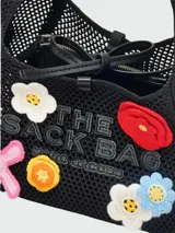 Bolso negro tejido al crochet con apliques de flores de colores y logo de la marca en el frente.