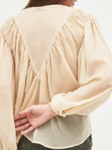 Blusa color crema con cuello redondo, botones frontales y mangas largas abullonadas.