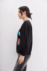 Buzo negro de algodón con cuello redondo y mangas largas abullonadas. Presenta apliques de flores bordadas con lentejuelas.