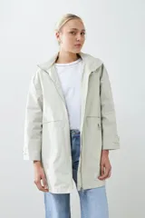 Campera impermeable gris claro con capucha plegable y bolsillos laterales.