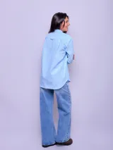 Camisa blanca de algodón, corte holgado, con cuello clásico y botones frontales. Las mangas son largas y se ven remangadas.