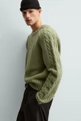 Sweater verde claro de punto con cuello redondo y mangas largas. Presenta diseño de trenzas en el centro y en las mangas.