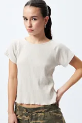Remera color beige de punto acanalado con silueta relajada y manga corta raglán. El detalle de ruedo con terminación ondulada le aporta un aire fresco y juvenil.
