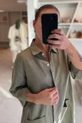 Vestido camisero color celeste de lino, con cuello clásico, cierre frontal con botones y mangas 3/4. Tiene dos bolsillos de parche en el pecho y corte irregular en el ruedo.