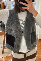 Chaleco marrón de cuero con interior de corderito color crema, cierre con gancho metálico y bolsillos frontales de corderito.