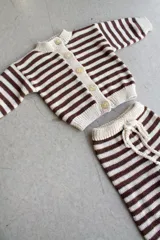 Conjunto tejido artesanalmente en hilado 70% algodón y 30% acrílico, compuesto por un cárdigan a rayas horizontales marrones y beige con botones y un pantalón a juego con cordón en la cintura.