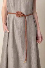 Cinto fino color beige, trenzado, con detalle de flor tejida al crochet.