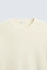 Jersey color crema de punto perlado, con cuello redondo, manga larga y corte regular fit.