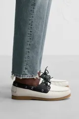 Zapato náutico de cuero blanco con detalles en negro y suela marrón.
