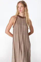 Vestido largo de tejido de punto fino con Lurex, de silueta en A, sin mangas y cuello halter. Presenta un patrón de rayas verticales en tonos beige y marrón oscuro.