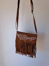 Bandolera marrón con flecos largos y apliques plateados en la solapa.